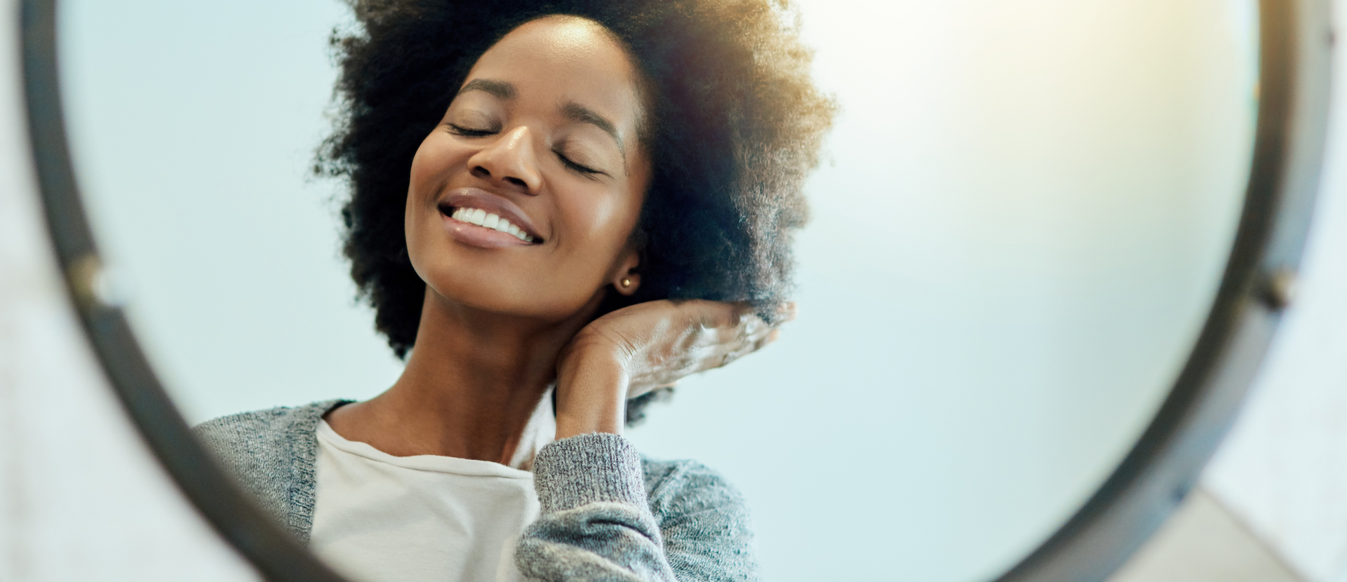 Zufriedene Frau mit lockigem Haar betrachtet sich lächelnd im Spiegel