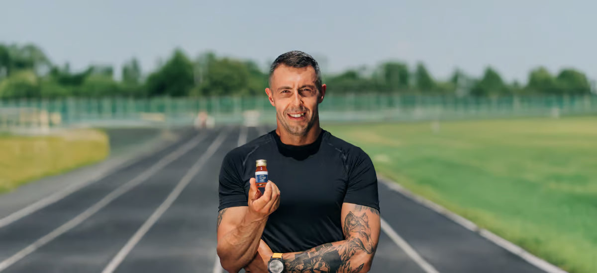 Der lächelnde Jurand Czabański steht mit einer Flasche Kollagen im Hintergrund eines Leichtathletikstadions.
