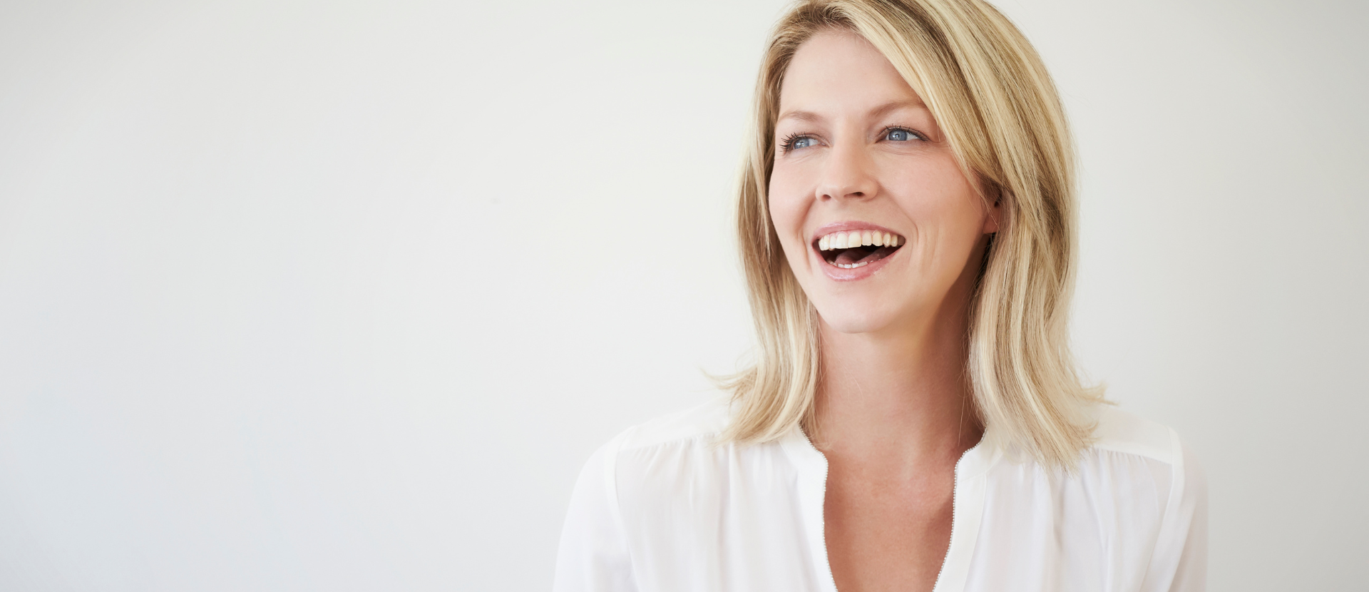 Fröhliche blonde Frau in weißer Bluse lächelt und schaut zur Seite