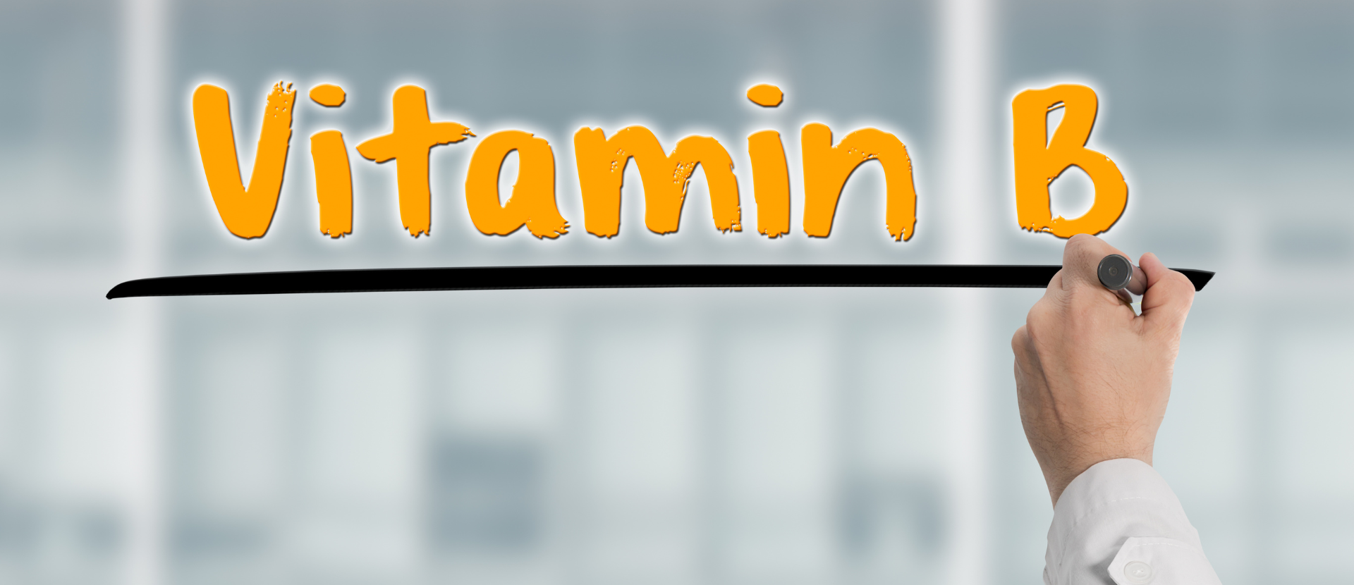 Hand eines Arztes unterstreicht den orangefarbenen Schriftzug „Vitamin B“ auf Glaswand