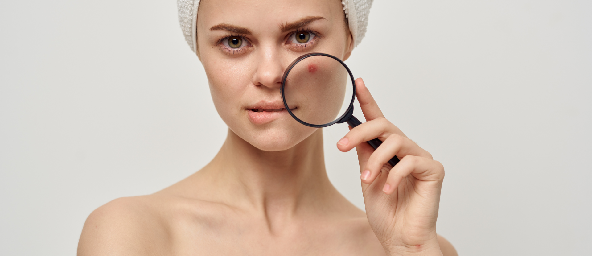Frau mit Handtuchturban betrachtet Mitesser auf ihrer Nase durch eine Lupe