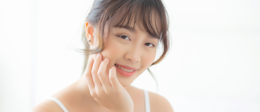 Junge Frau mit zarter, strahlender Haut lächelt und berührt sanft ihre Wange