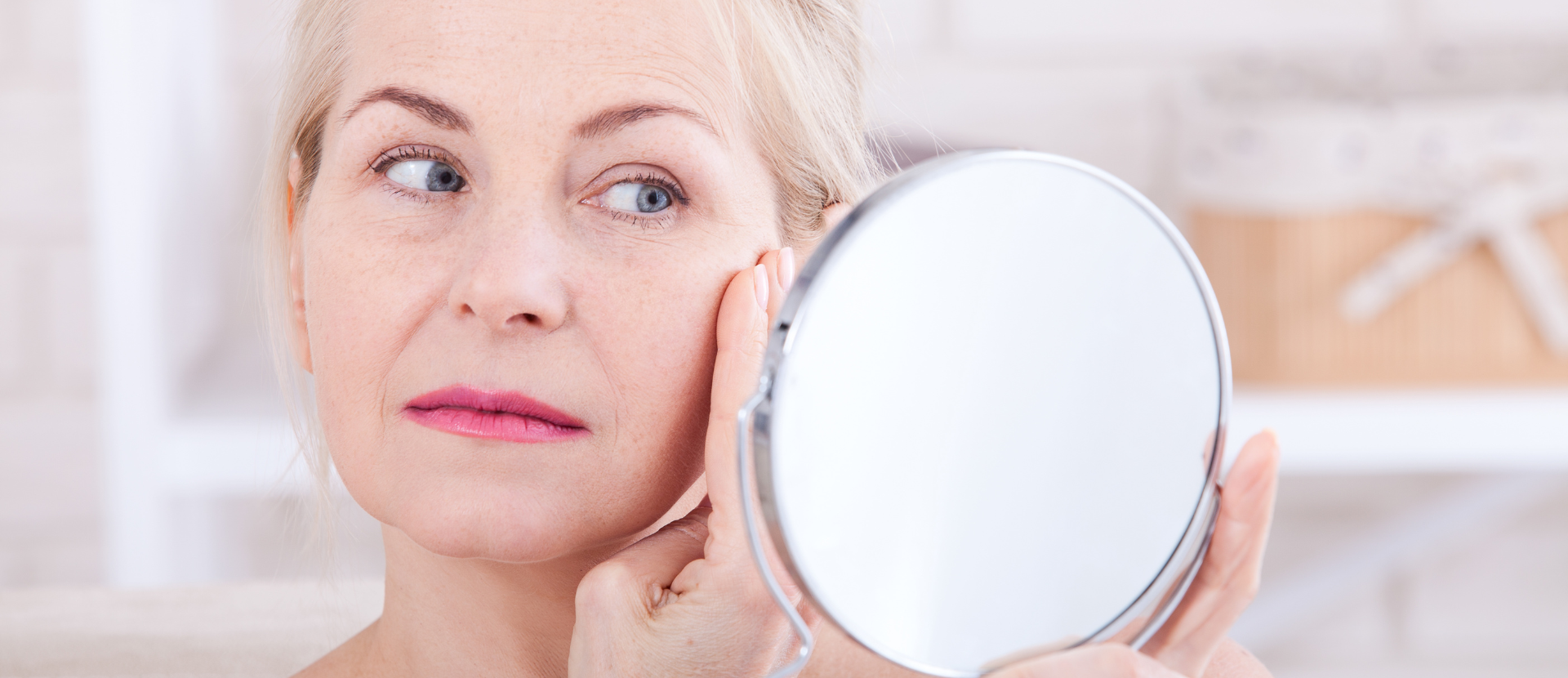 Reife Frau betrachtet ihr Gesicht im Spiegel und prüft ihre Hautbeschaffenheit
