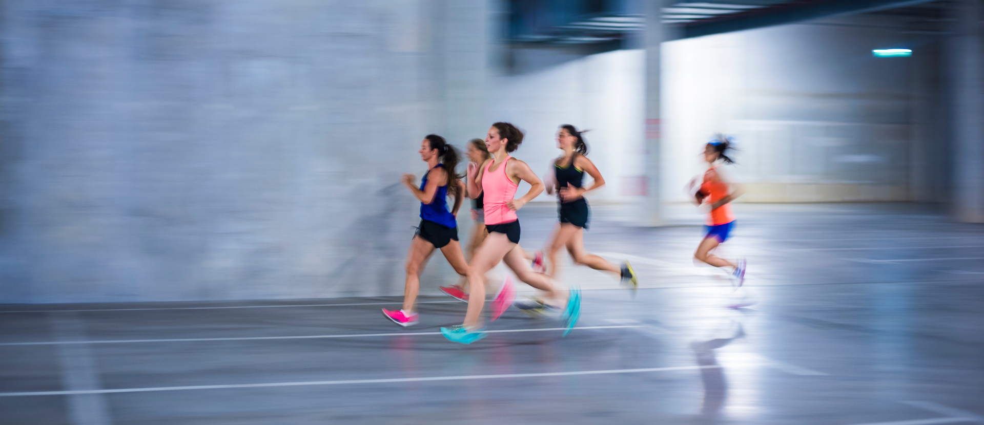 Gruppe sportlicher Frauen läuft gemeinsam in heller Sportkleidung durch eine Halle