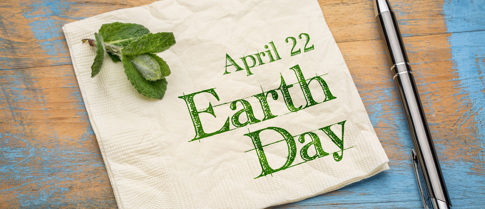 Serviette mit Aufschrift „Earth Day April 22“ auf Holztisch neben Stift und Minzblättern