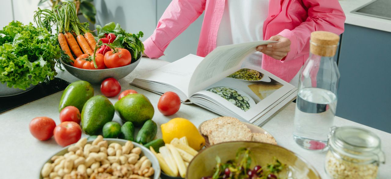 Person blättert in einem Kochbuch neben frischem Gemüse auf dem Tisch, passend für Ernährung nach den Feiertagen