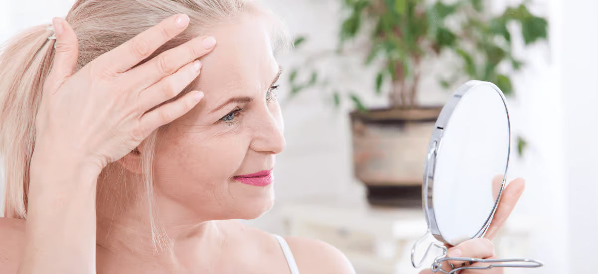 Eine lächelnde Frau, die sich im Spiegel betrachtet.