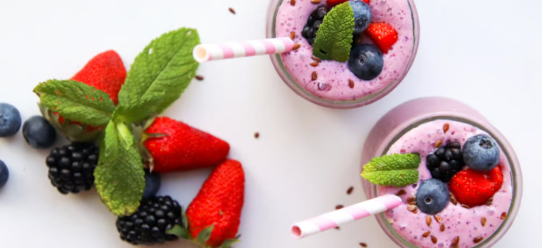 Ein gesunder Smoothie in drei Gläsern mit Strohhalmen, die mit Früchten wie Erdbeere, Heidelbeere und Brombeere dekoriert sind.