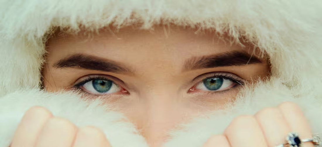 Nahaufnahme einer Frau mit blauen Augen, eingehüllt in weiches weißes Fell, die ihr Gesicht vor winterlicher Kälte schützt.