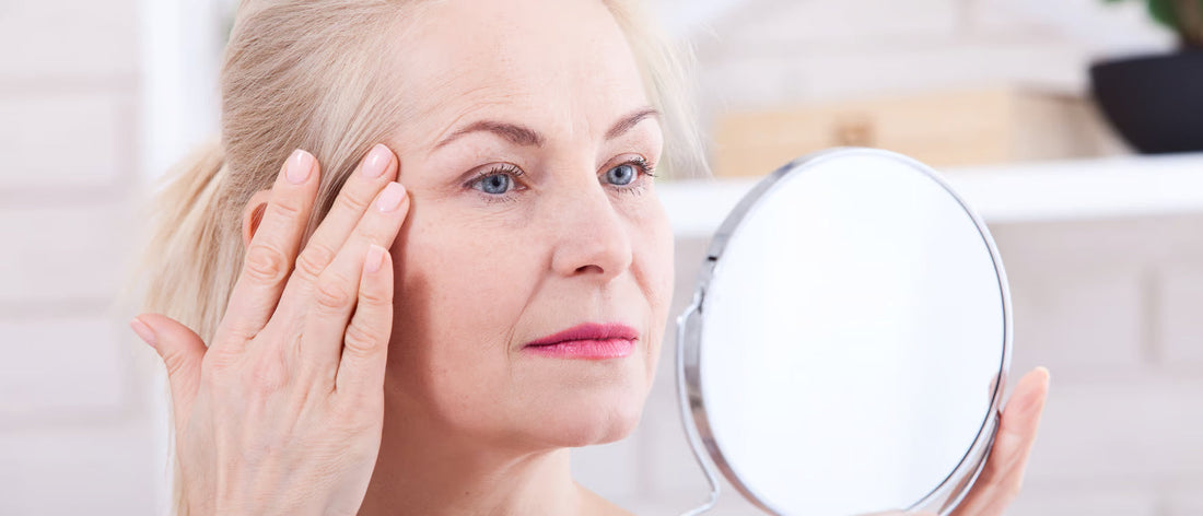 Frau betrachtet im Spiegel ihre Gesichtshaut und berührt Falten vor der Anwendung von Primabiotic Kollagen
