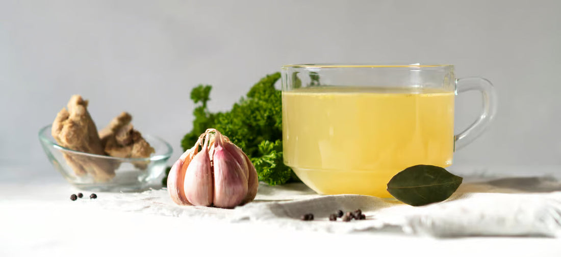 Kollagenbrühe in einem Glas, dazu Knoblauch, Ingwer und Gewürze