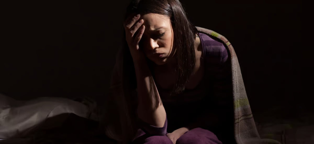 Eine traurige Frau, die sich aufgrund von Schlaflosigkeit den Kopf hält.