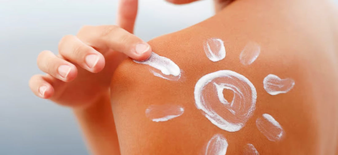 Die Hand, die den Rücken mit Sonnencreme eincremt und mit der Creme eine Sonne darauf malt.