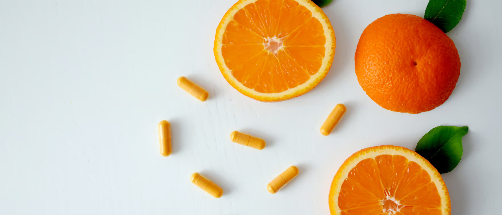 Aufgeschnittene Orangen und verstreute Vitamin-C-Kapseln auf weißem Hintergrund.