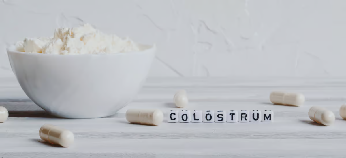 Kapseln und Pulver aus bovinem Kolostrum neben dem Schriftzug „Colostrum“ auf hellem Hintergrund