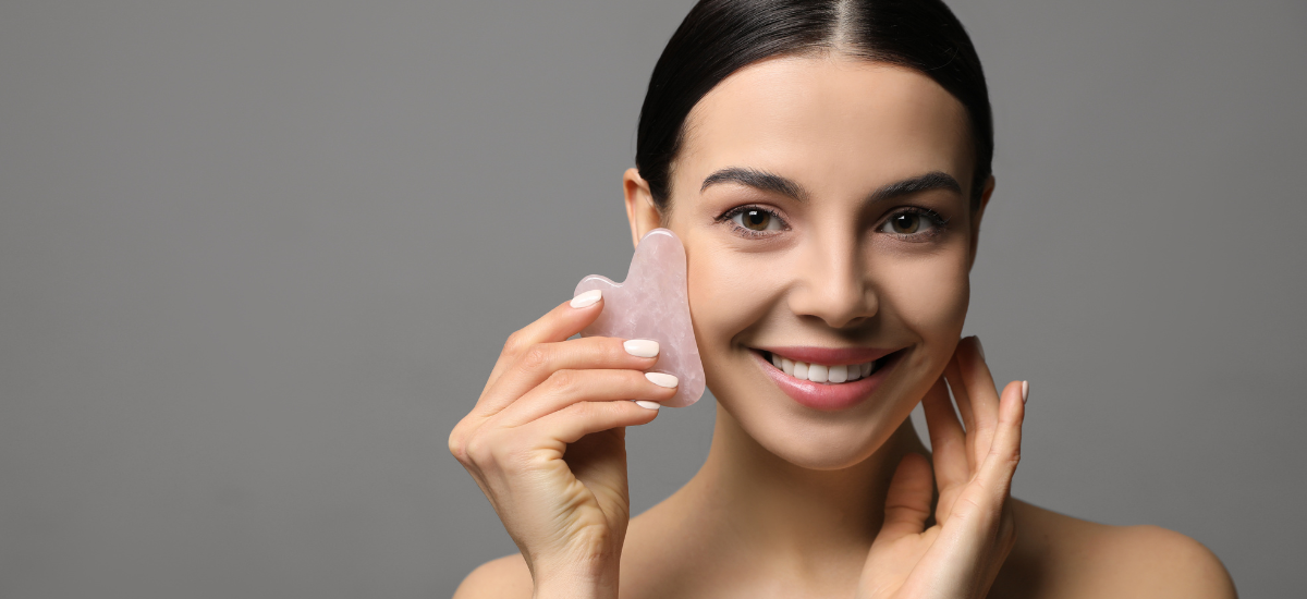 Lächelnde Frau massiert ihr Gesicht mit einem rosa Gua-Sha-Stein für strahlende Haut