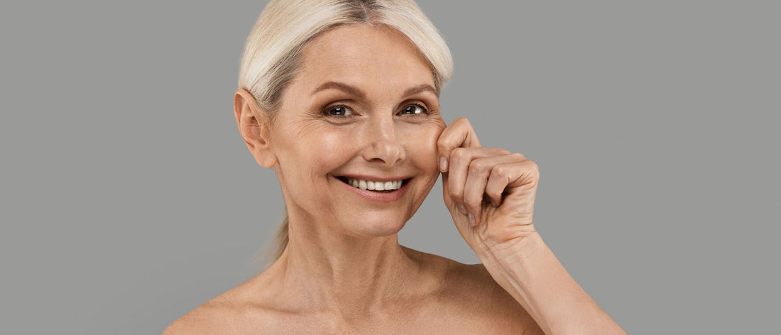 Lächelnde reife Frau berührt ihre Wange und zeigt die Wirkung der Primabiotic Kollagen-Supplementierung bei schlaffer Haut