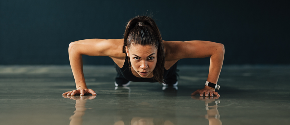 Entschlossene Frau macht Liegestütze auf glänzendem Boden im Fitnessstudio