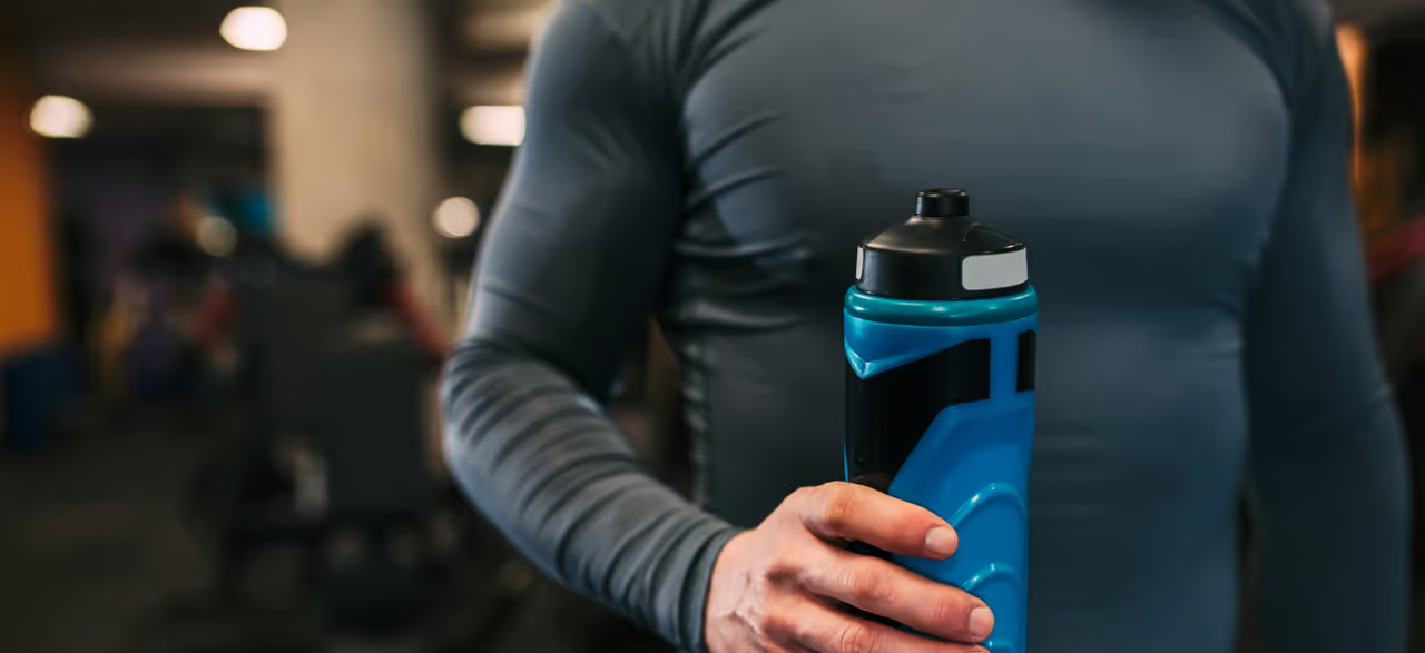 Mann in Sportkleidung mit Bidon in der Hand