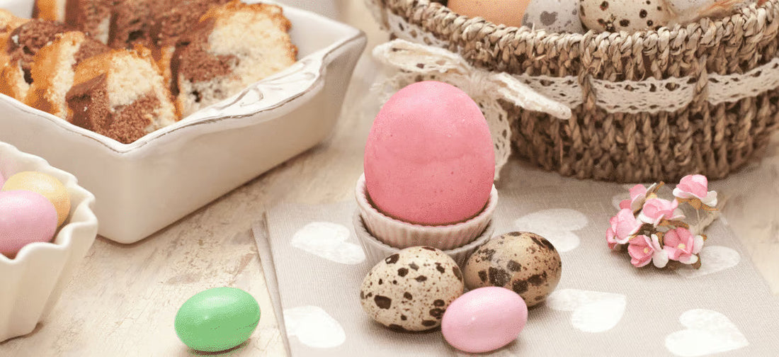 Osterdekoration mit rosa Ei, Wachteleiern, Kuchenstücken und geflochtenem Korb auf festlichem Tisch