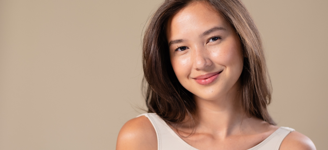 Junge Frau mit natürlichem Make-up und glatter, strahlender Haut lächelt sanft in die Kamera