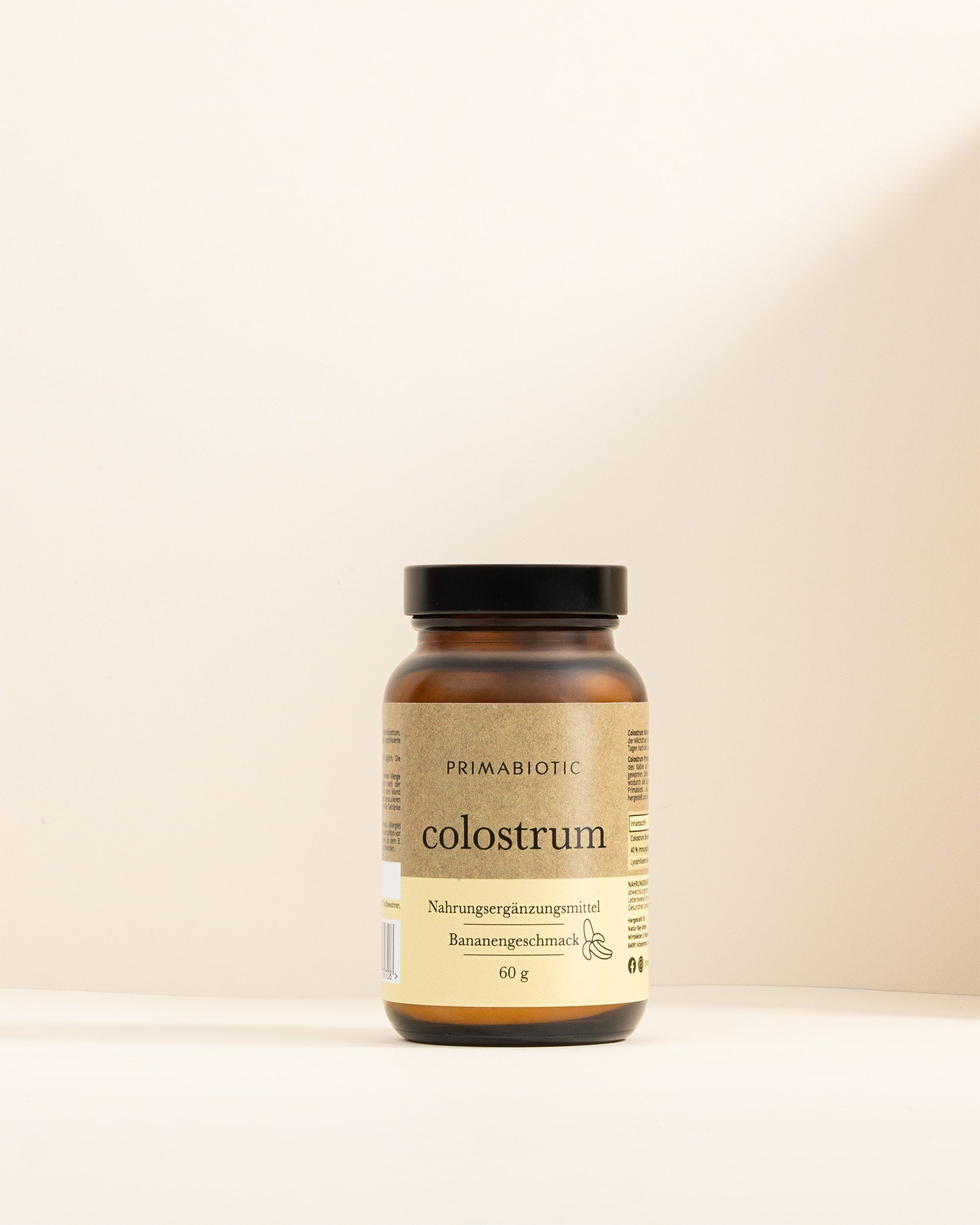 Glasbehälter Primabiotic Colostrum Bananengeschmack 60 g steht auf hellem Hintergrund.