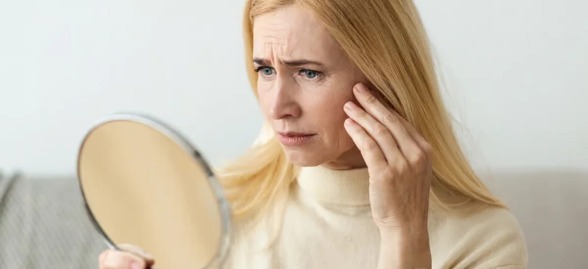 Eine Frau betrachtet ihr Gesicht im Spiegel und runzelt die Stirn