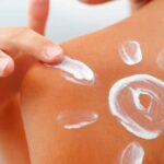 Die Hand, die den Rücken mit Sonnencreme eincremt und mit der Creme eine Sonne darauf malt.